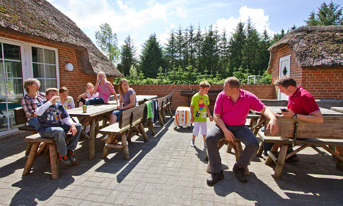 Blick auf große Terrasse eines Gruppenferienhauses mit Menschen und Gartenmöbeln