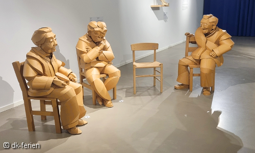 Blick auf eine Sitzgruppe mit 3 Figuren aus Vollpappe im Museum für Papierkunst in Blokhus